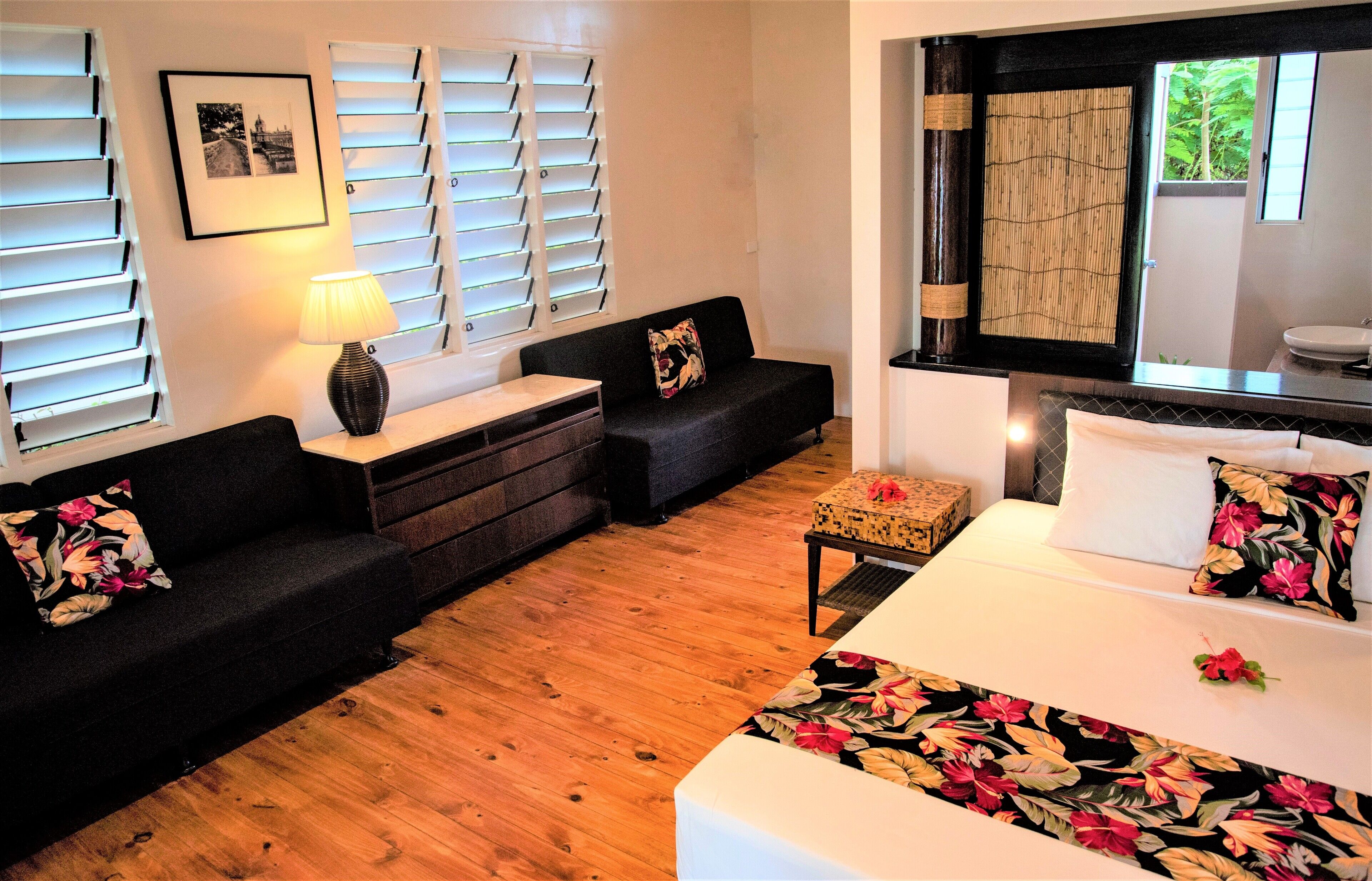A hotel room with a bed, two sofas, a small table, and a window with blinds.