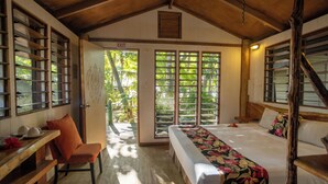 Ein Zimmer mit einem Bett, einem Schreibtisch und einem Sessel. Eine Tür und ein Fenster mit Blick auf Bäume sind vorhanden.