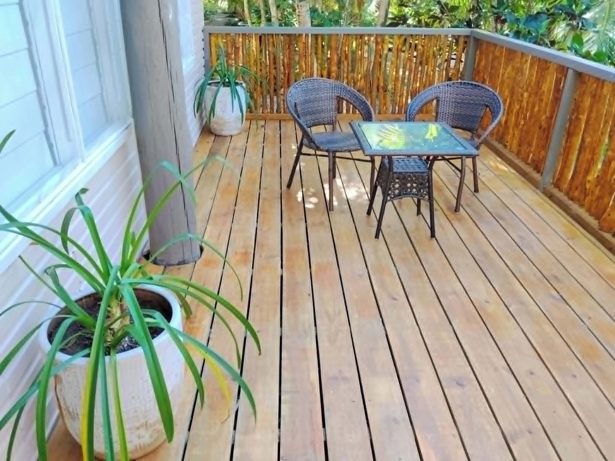 A wooden deck with two wicker chairs and a table, surrounded by a bamboo fence.
