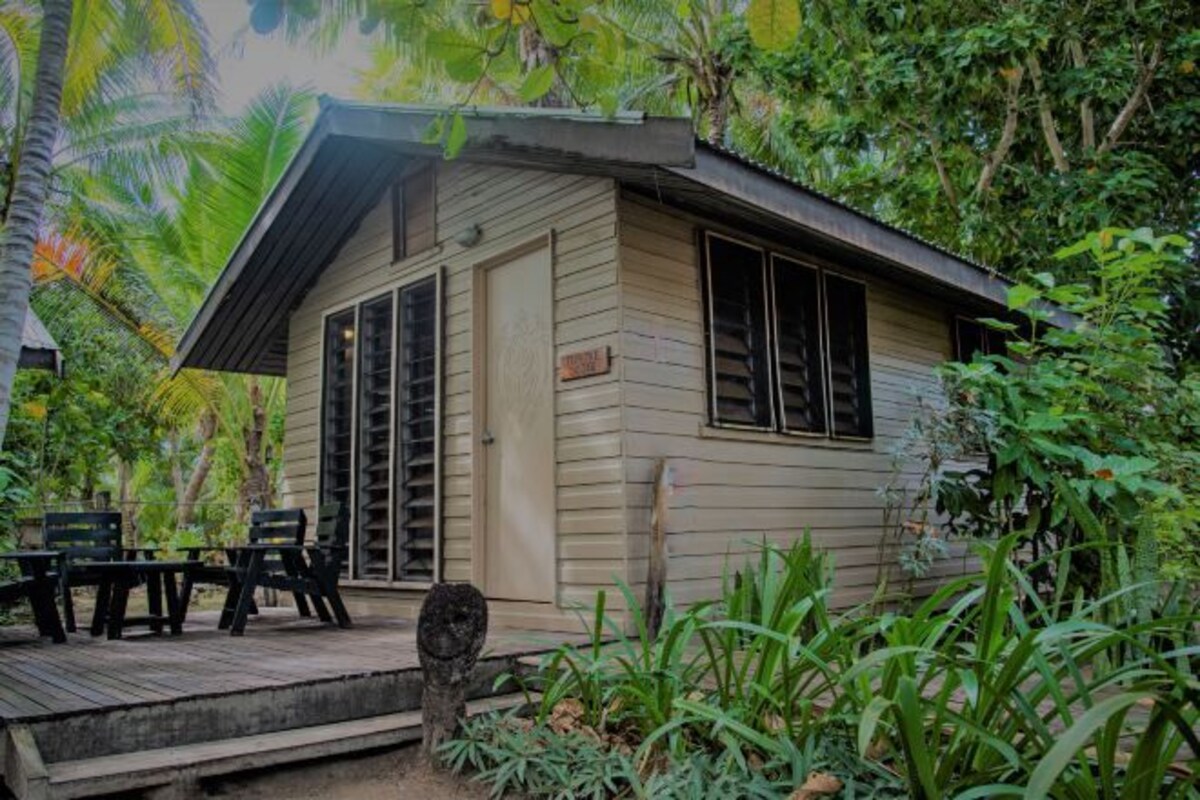 Une cabane en bois dotée d’une terrasse, entourée d’une végétation tropicale.