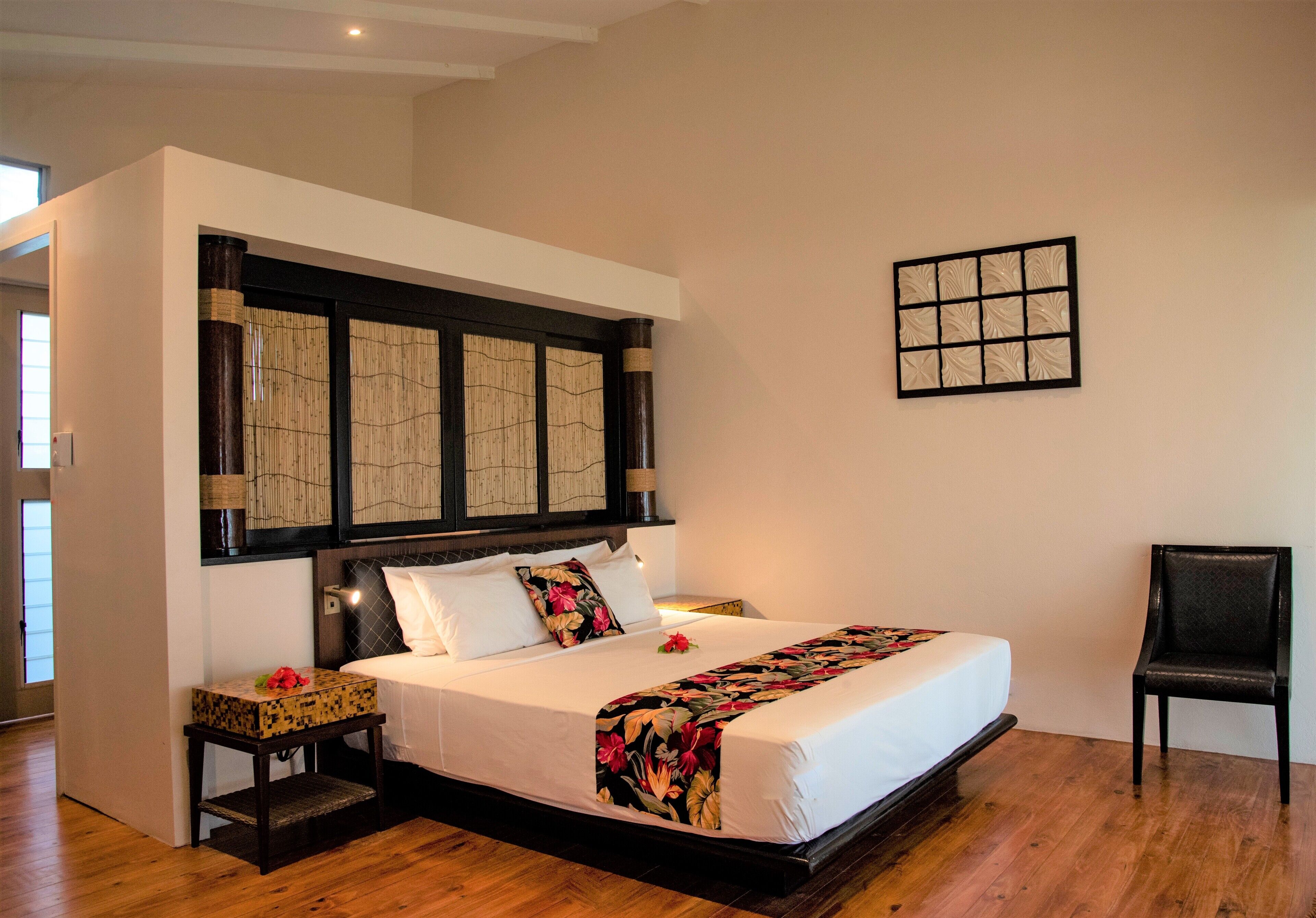 Un dormitorio ordenado con cama, mesitas de noche, una silla y un adorno en la pared.