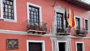 A building with a red facade, multiple windows, and balconies with potted plants. - Hotel NASS Casa del Aguila (Cuenca)