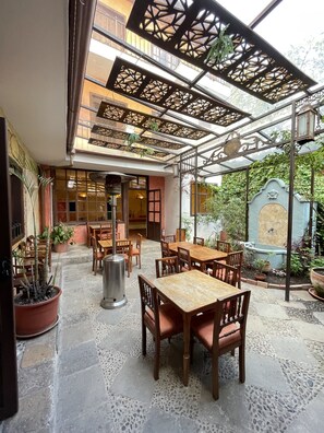 An outdoor patio with wooden tables and chairs, potted plants, and a decorative metal ceiling.
