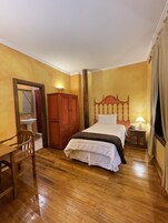 Quarto com cama de madeira, guarda-roupa de madeira, mesa de cabeceira com abajur e uma cadeira.