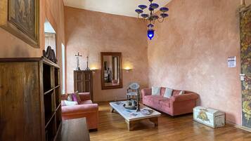 A spacious living room with wooden flooring, a chandelier, a pink sofa, and a wooden cabinet.