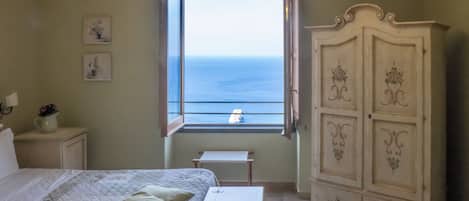 A bedroom with a bed, a nightstand, a dresser, a window with a view of the sea, and a chandelier.