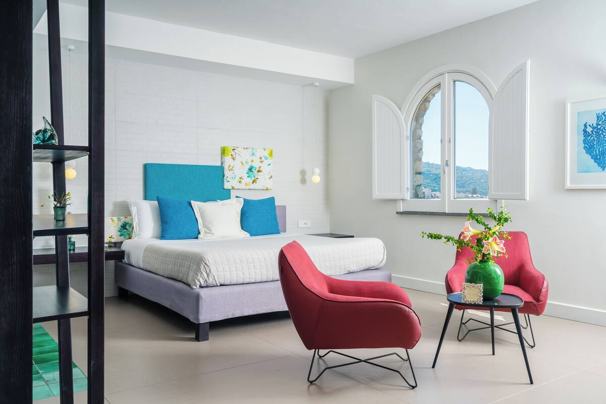 Ein modernes Schlafzimmer mit einem Bett, einem roten Sessel, einem kleinen Tisch mit einer Vase und einem Fenster mit bogenförmigem Design.