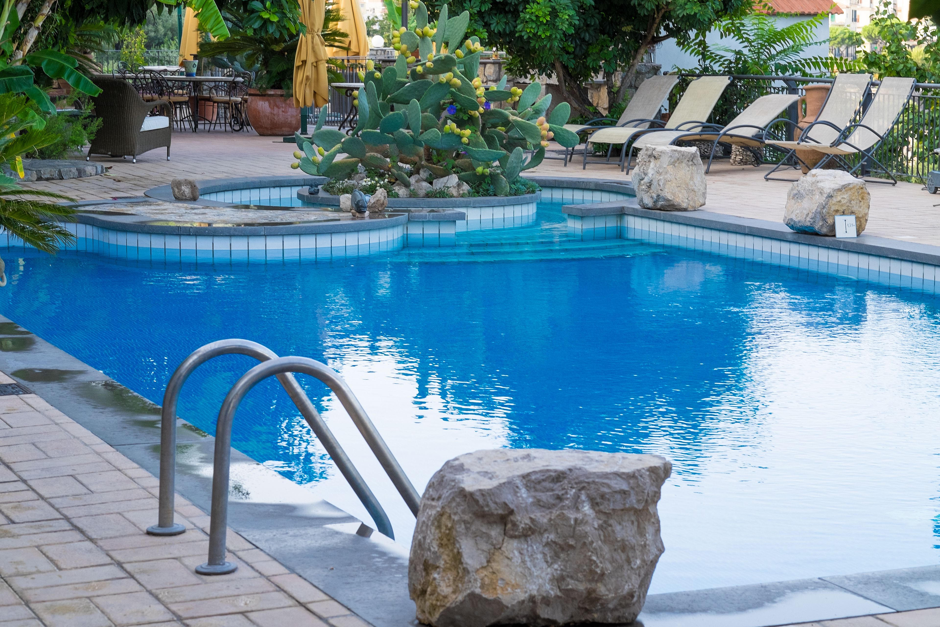 A pool with a clear blue water, surrounded by lounge chairs and a cactus plant.