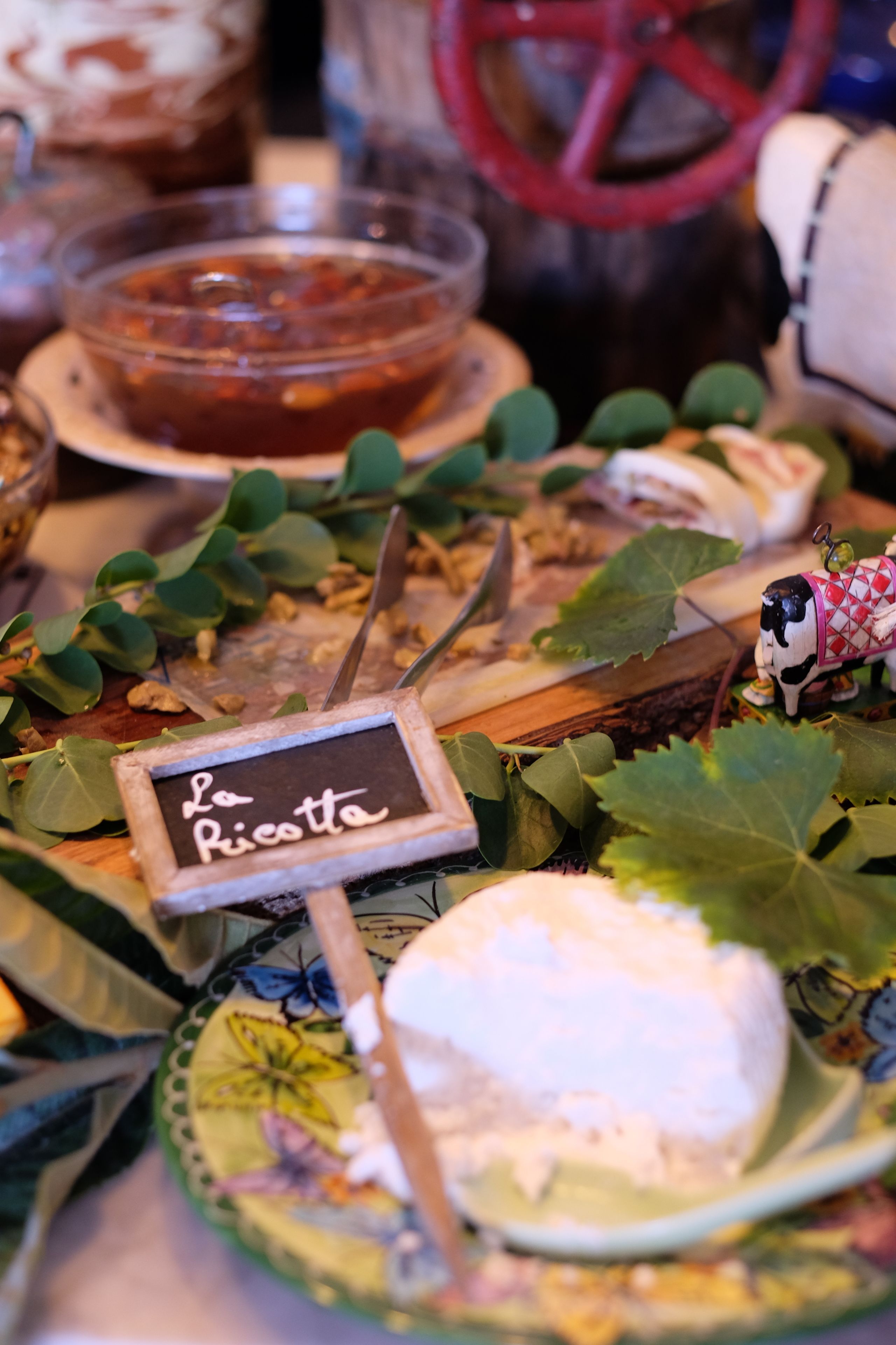 A cheese board with a sign reading "La Ricotte" surrounded by leaves and a small figurine.