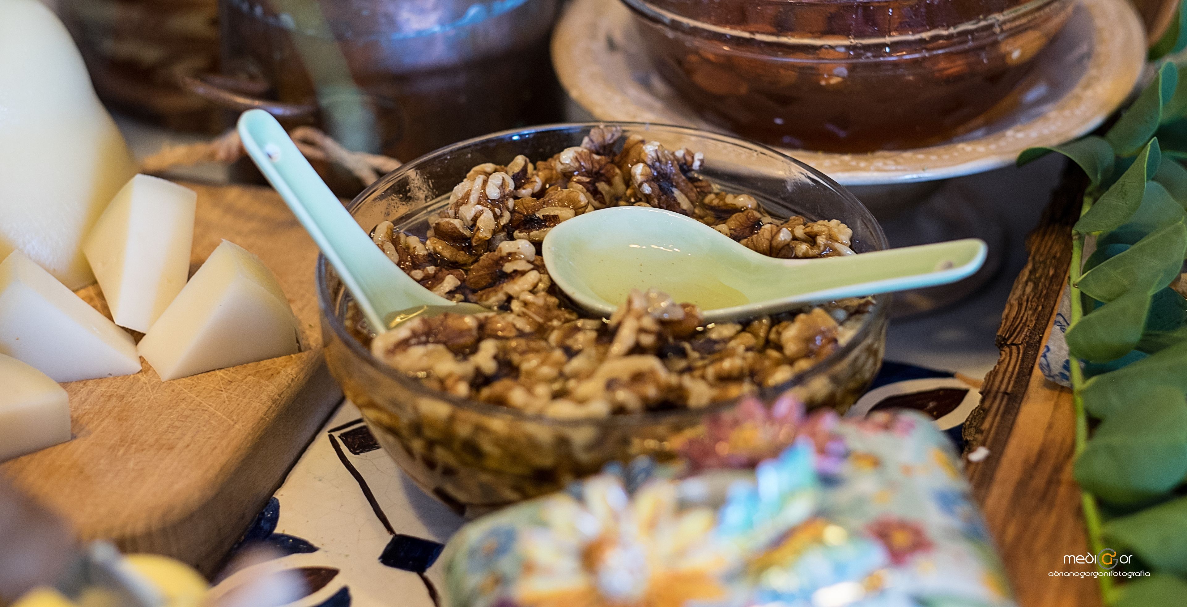 Un tazón de granola con nueces y una cuchara, una tabla de madera con rodajas de manzana, y un frasco de mermelada de colores.