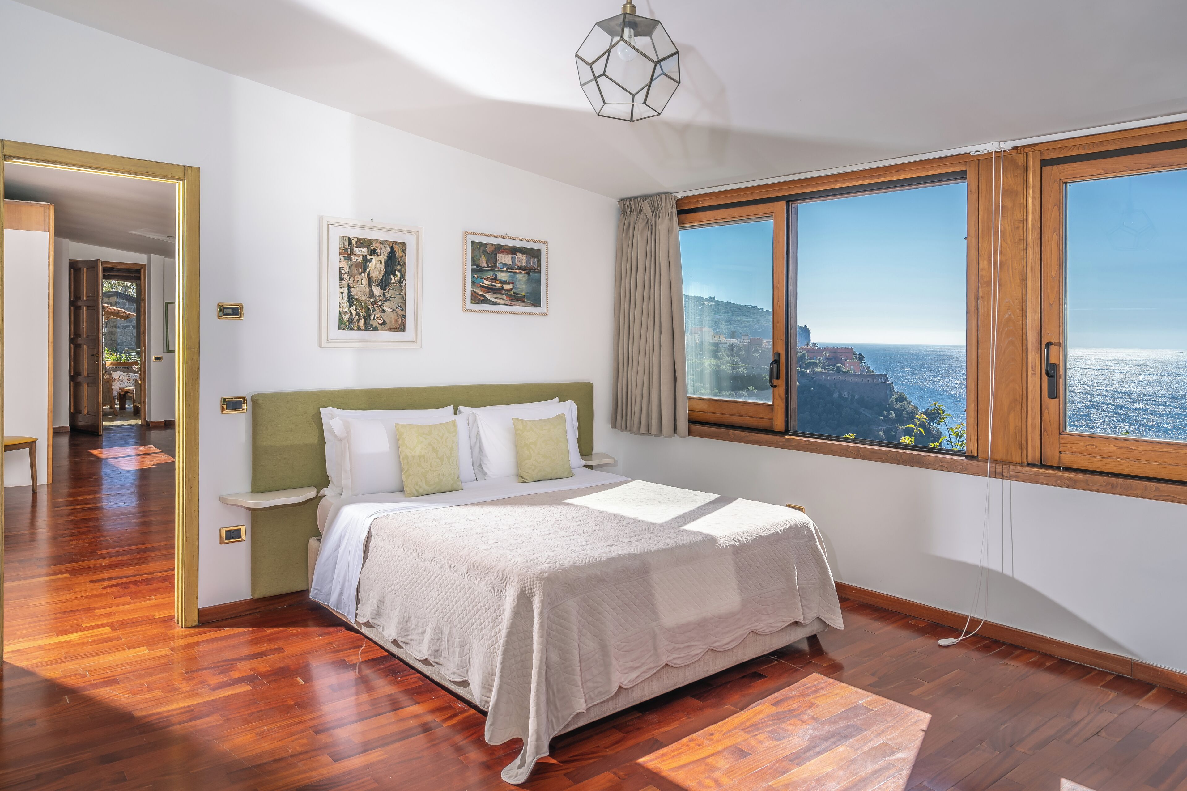 A bedroom with a large bed, a view of the sea, and a wooden floor.