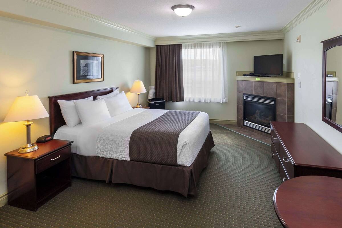 A hotel room with a large bed, a television, a fireplace, and a desk with a chair.