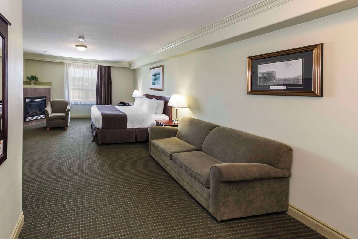 A hotel room with a bed, a sofa, a chair, a fireplace, and a framed picture on the wall.