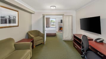 Quarto de hotel com uma cama, televisão, secretária com telefone e duas cadeiras.
