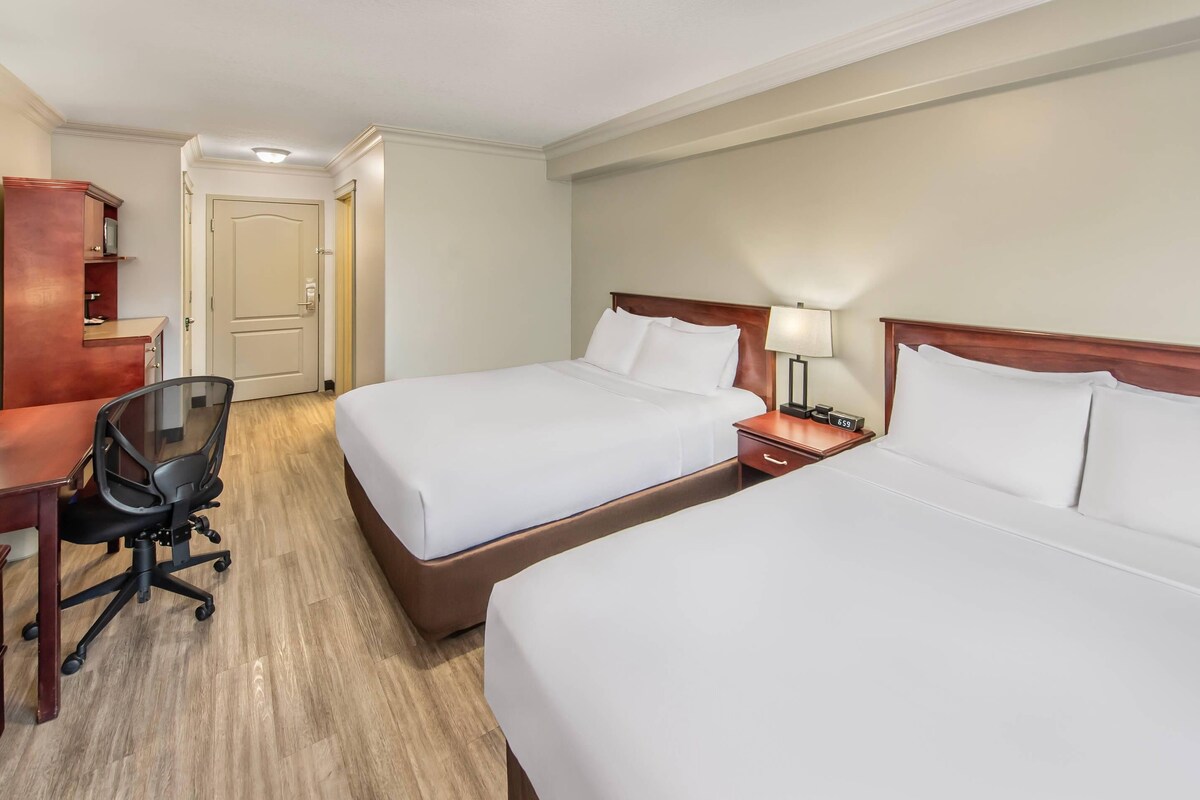 Une chambre d’hôtel avec deux lits, un bureau, une chaise et une table de chevet avec une lampe.
