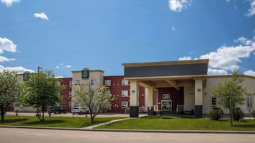 Hotel entrance with a covered area and flat roof, surrounded by trees and a well-manicured lawn.