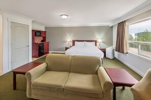 A hotel room with a bed, a sofa, a desk, a microwave, and a window with a view. - Quality Inn & Suites Whitecourt (Whitecourt)