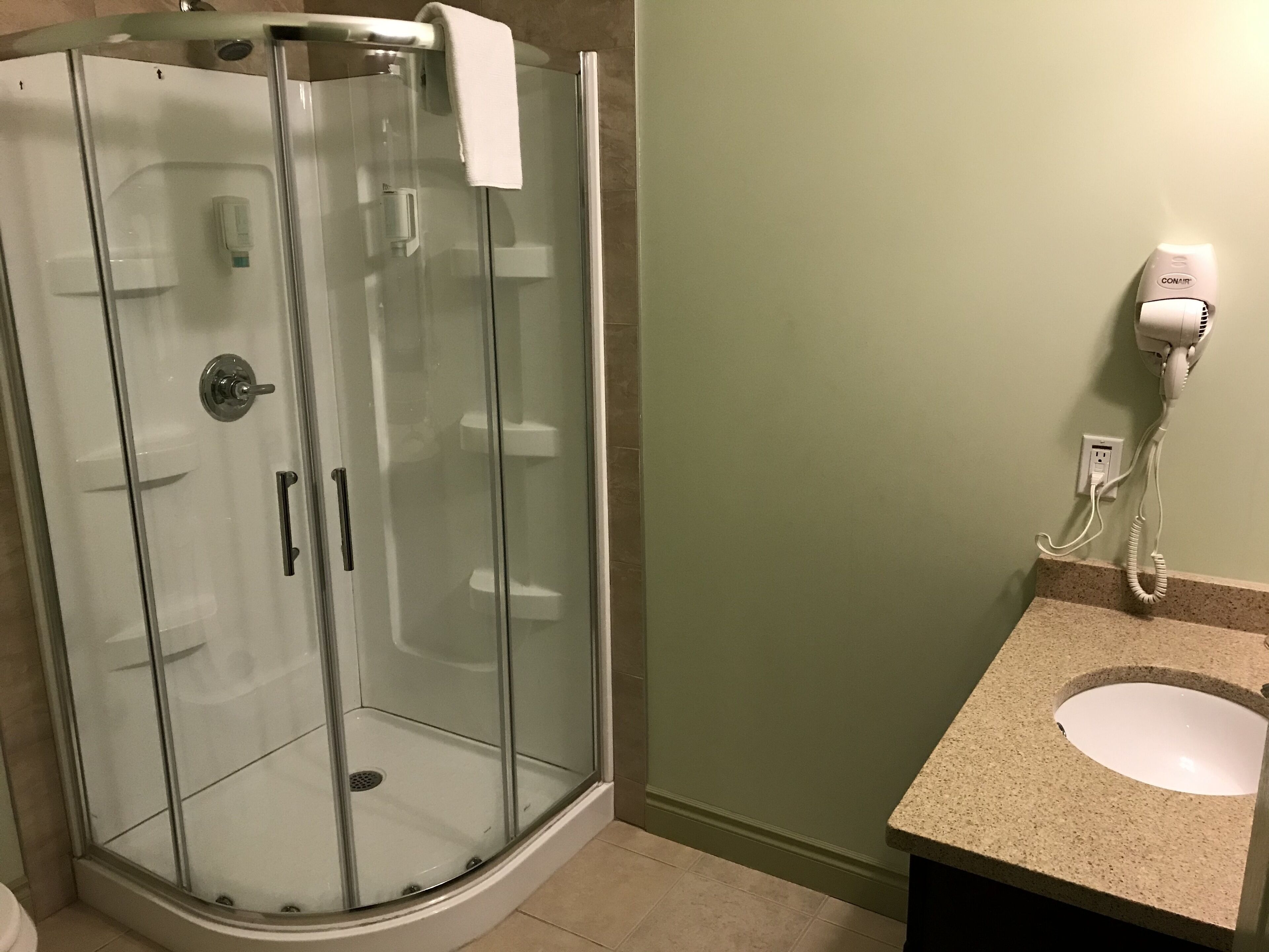 A glass-enclosed shower with a towel rack, a hairdryer on the wall, and a sink with a granite countertop.