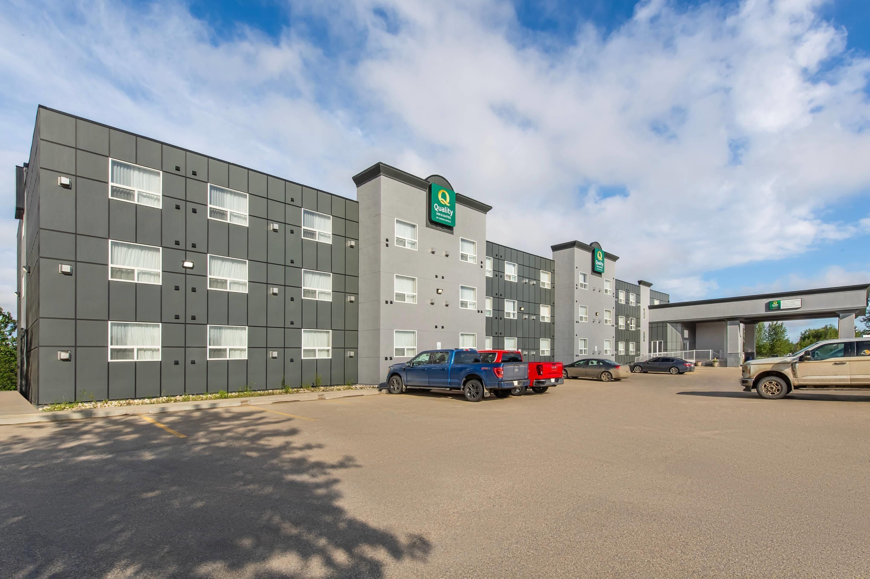 A modern hotel building with multiple floors, a parking lot, and a clear sky.