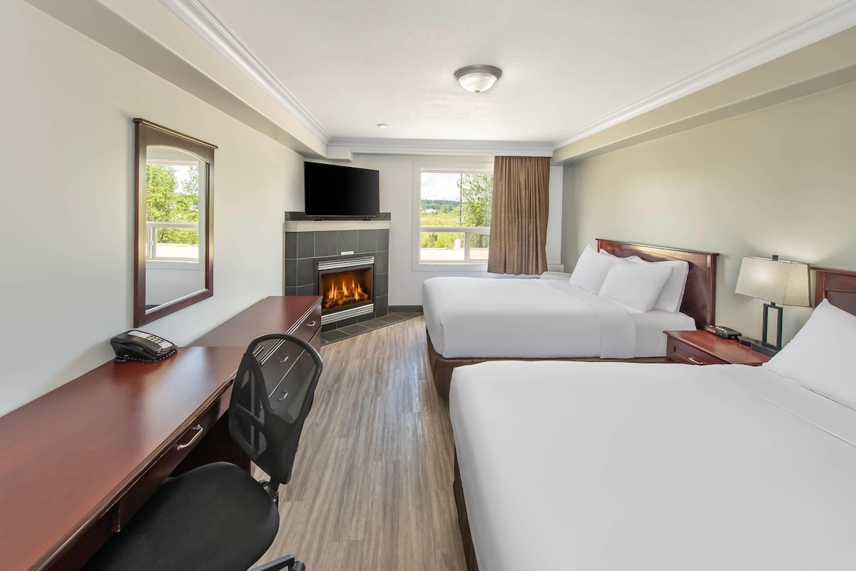 A hotel room with two beds, a desk with a chair, a fireplace, a TV, and a window with curtains.