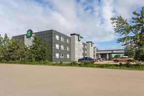 A hotel with a modern design, featuring multiple floors and a parking area with several vehicles. - Quality Inn & Suites Whitecourt (Whitecourt)