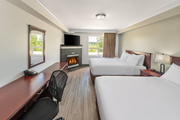 A hotel room with two beds, a desk, a chair, a TV, a fireplace, and a window with curtains.