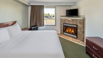 A hotel room with a bed, a fireplace, a television, and a window with curtains.