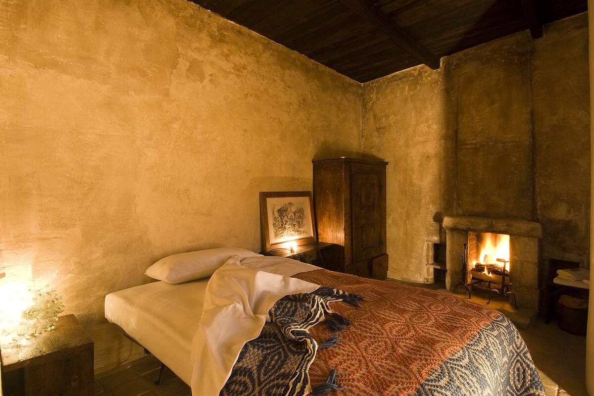 A bedroom with a bed, a wooden cabinet, a fireplace, and a framed picture on the wall.