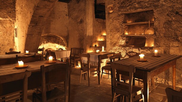 A rustic stone interior with wooden tables and chairs, a stone fireplace, and candle-lit ambiance. - Sextantio Albergo Diffuso (Santo Stefano di Sessanio)