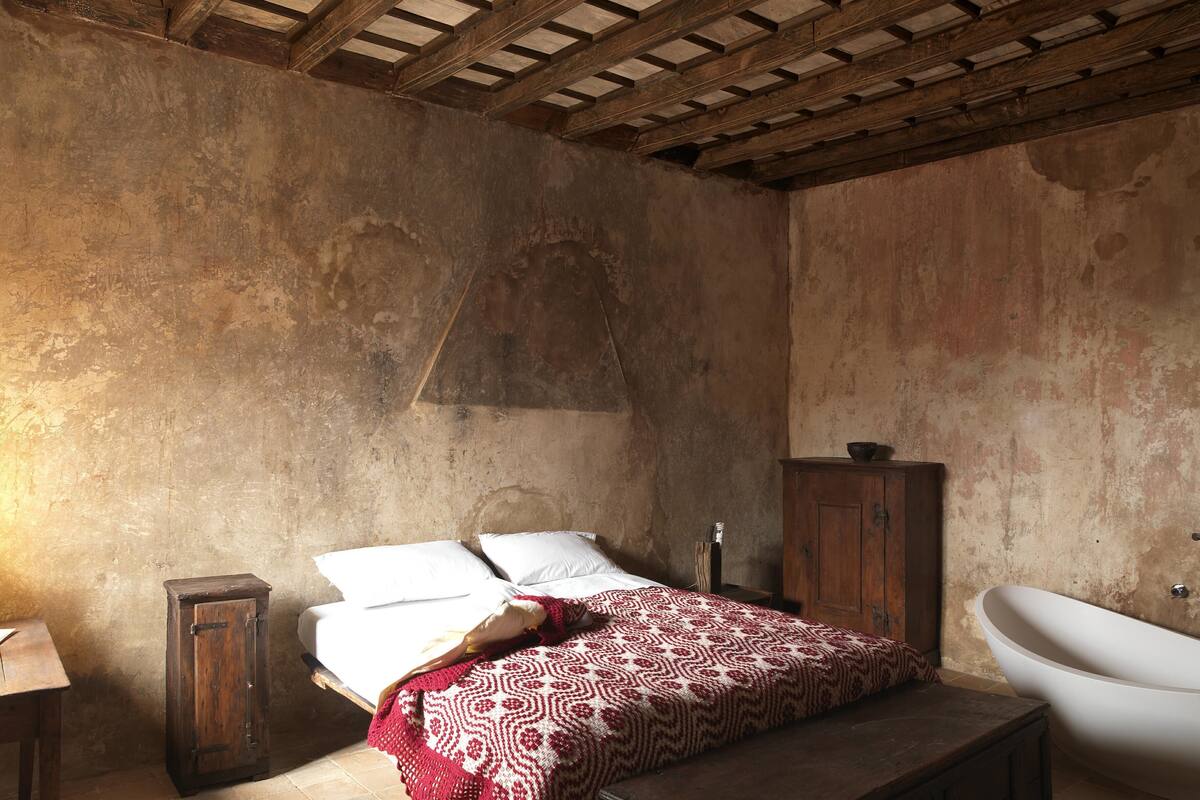 A rustic bedroom with a wooden bed, a wooden cabinet, and a white bathtub.