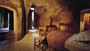 A rustic room with a wooden bed, a chair, and a desk with a mirror. - Sextantio Albergo Diffuso (Santo Stefano di Sessanio)