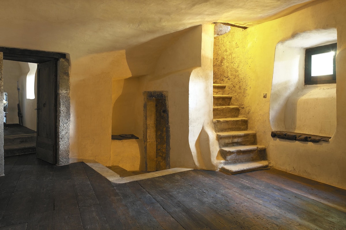 A room with a spiral staircase, wooden flooring, and a door leading to another area.