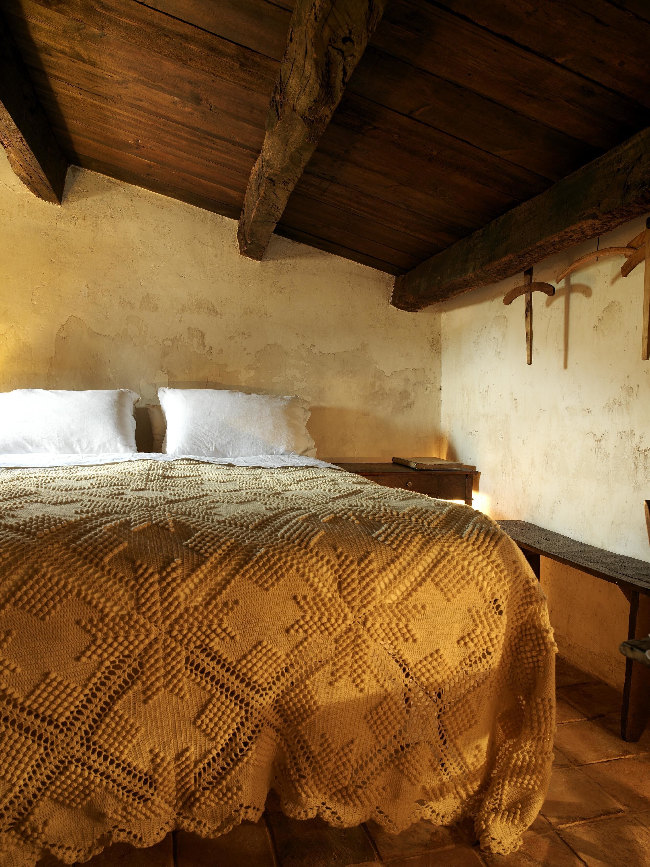 Una habitación rústica con techo de madera, una cama con ropa de cama blanca y una manta tejida.