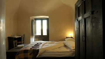 A bedroom with a bed, a desk, and a chair. There is a window with a view of the outside.