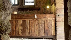 A rustic stone-walled room with a wooden bench, a television mounted on the wall, and a small shelf with various items. - Sextantio Albergo Diffuso (Santo Stefano di Sessanio)