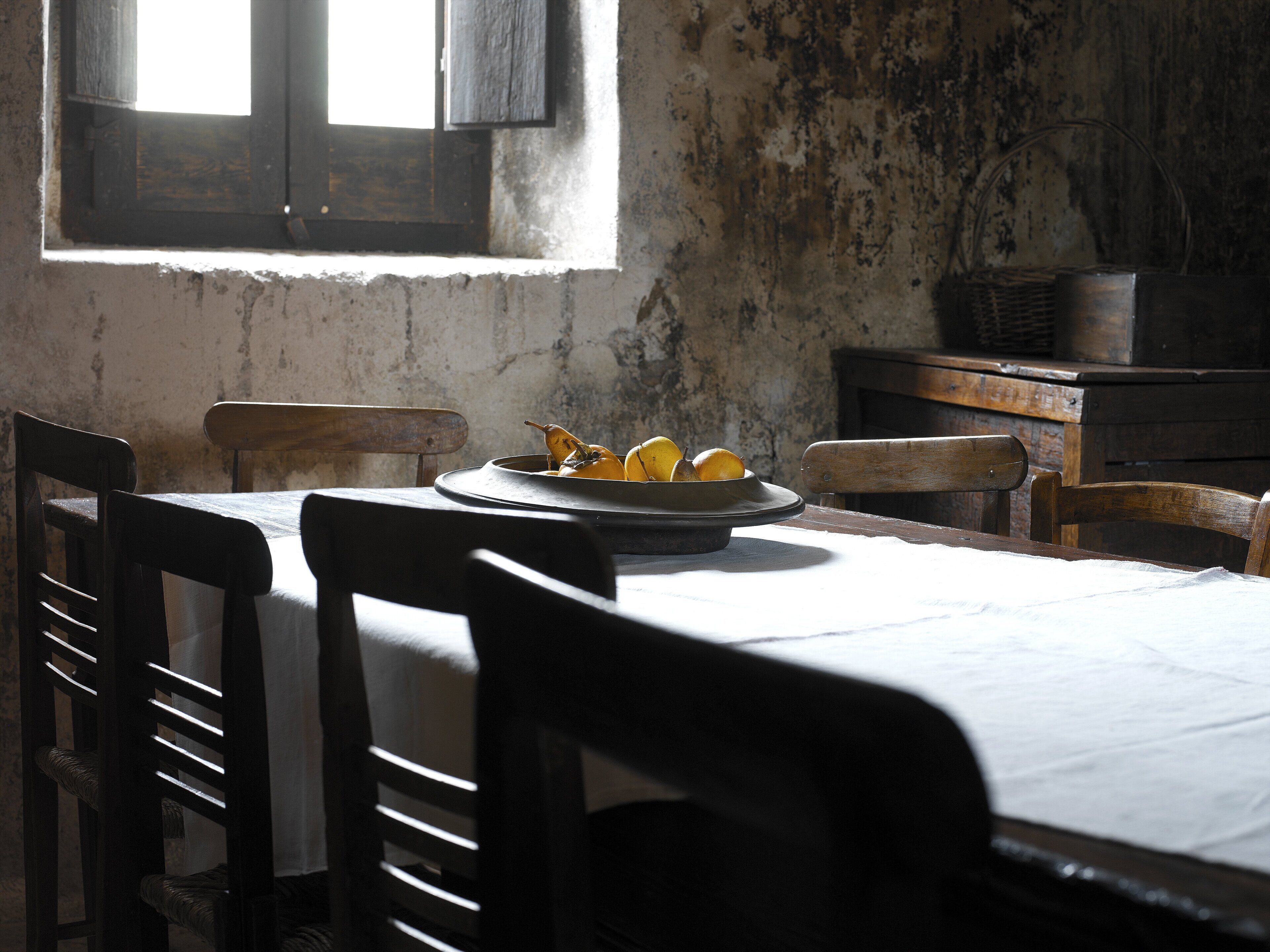 A rustic dining room with a table set for two, featuring a plate of lemons and a wicker basket.