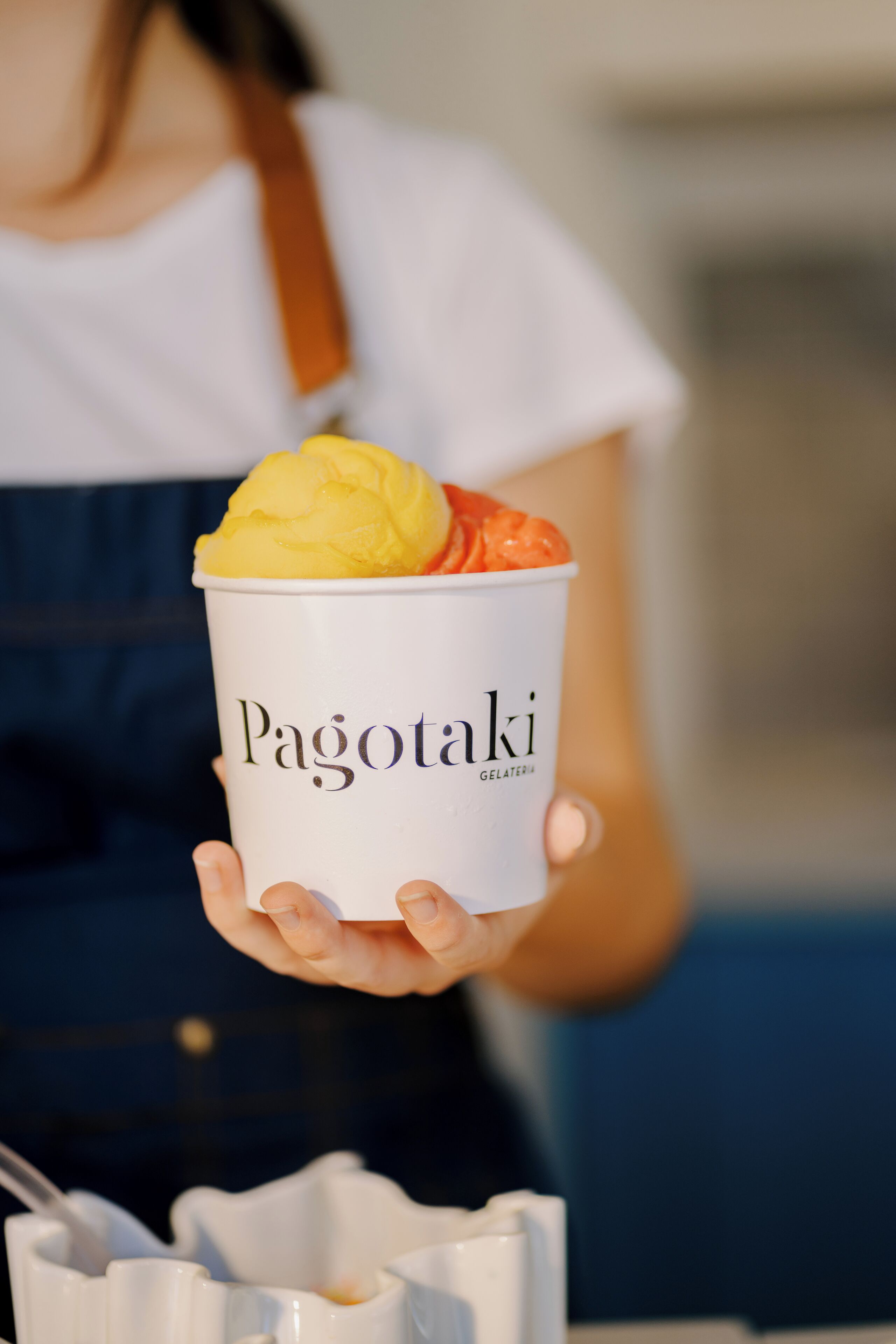 A person holding a cup of gelato with the brand name 'Pagotaki' visible on it.
