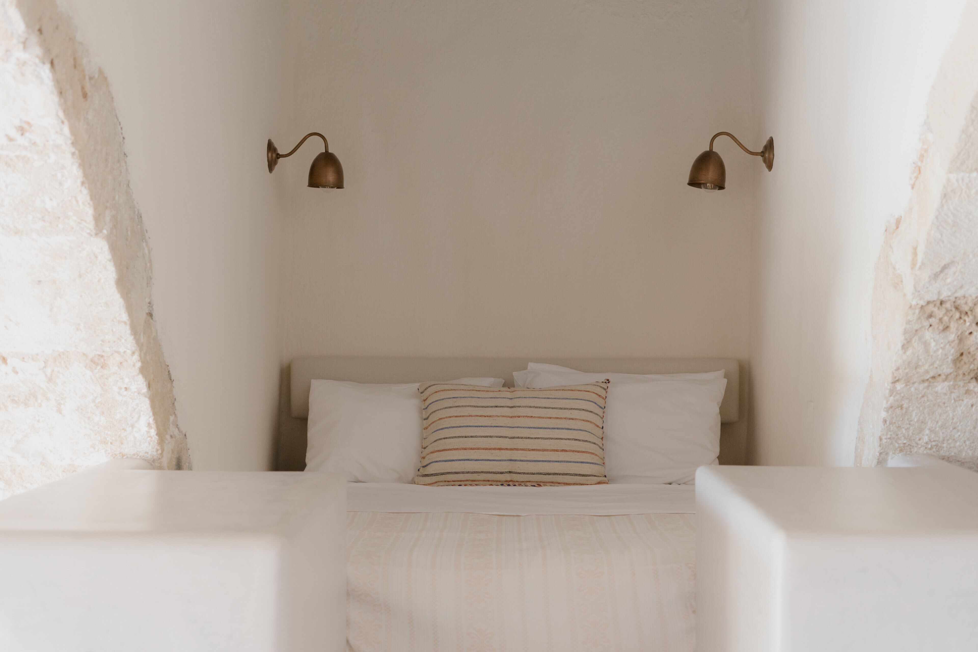 Un dormitorio con una cama, dos lámparas de pared y un cojín a rayas.