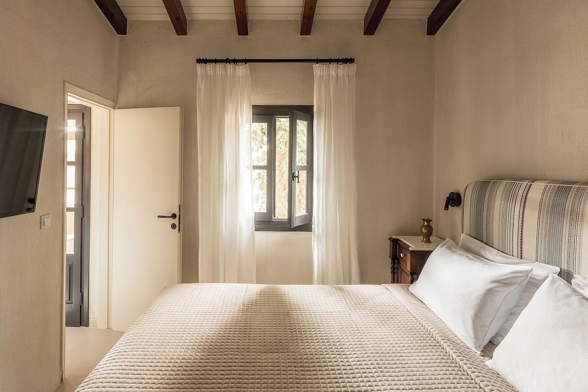 Une chambre à coucher avec un lit, une fenêtre avec des rideaux, une table de chevet avec une lampe et un téléviseur fixé au mur.