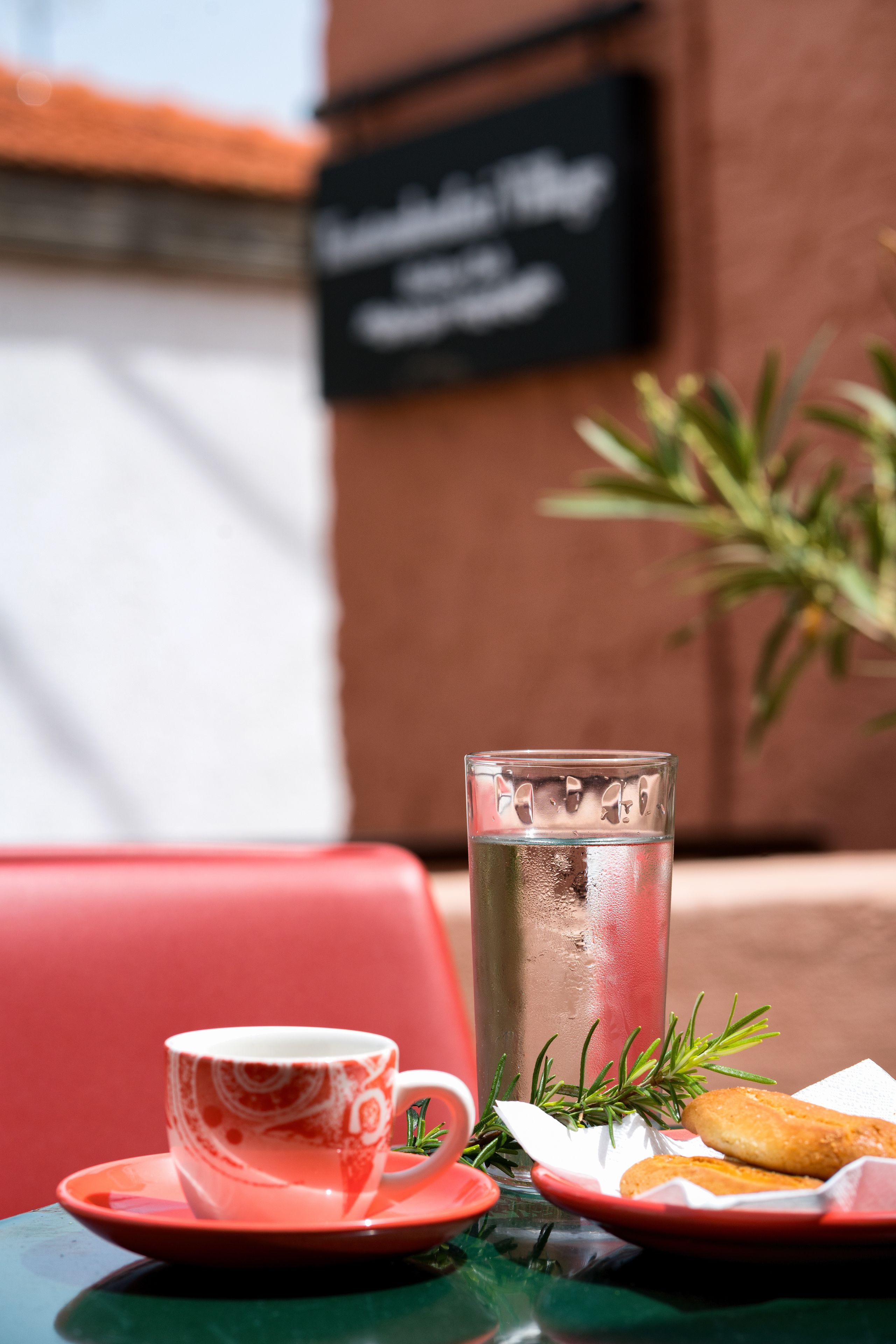 Una mesa con un vaso de agua, una taza y un pastel sobre un mantel rojo.