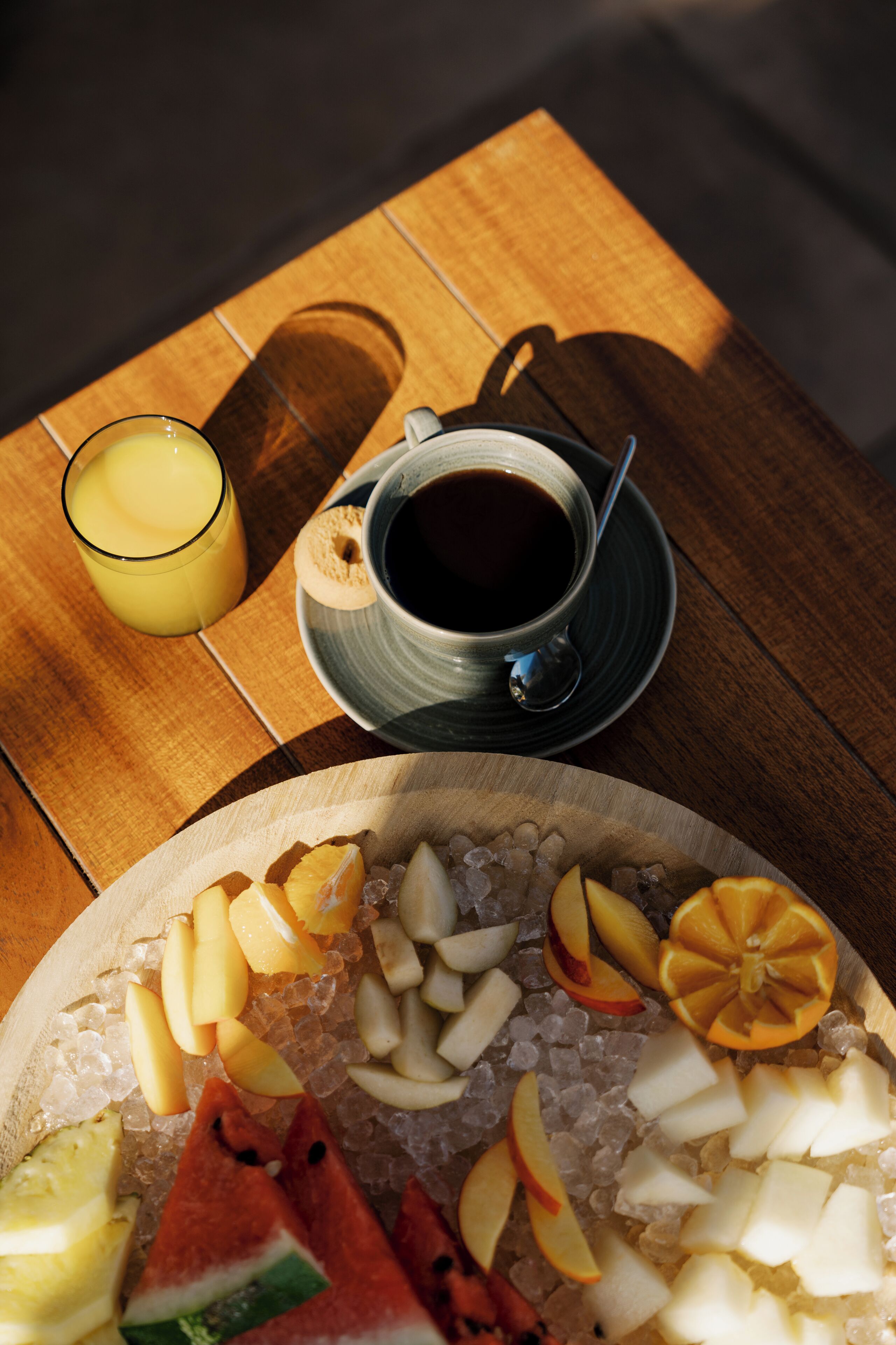 A wooden table with a plate of fruit and a cup of coffee.