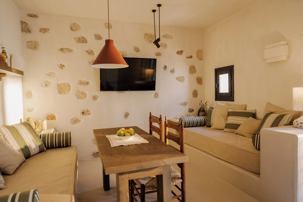 Ein gemütliches Wohnzimmer mit Holztisch, Sofa, an der Wand montiertem Fernseher und Wandgestaltung im Steinoptik.