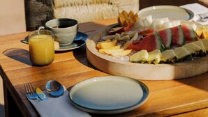 Una mesa de desayuno con una bandeja de fruta, un vaso de jugo de naranja y un tazón de sopa.