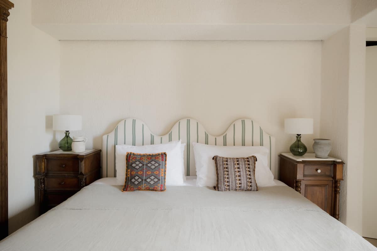 Un lit bien fait, avec deux oreillers et deux tables de chevet, chacune ornée d’une lampe et d’un vase.
