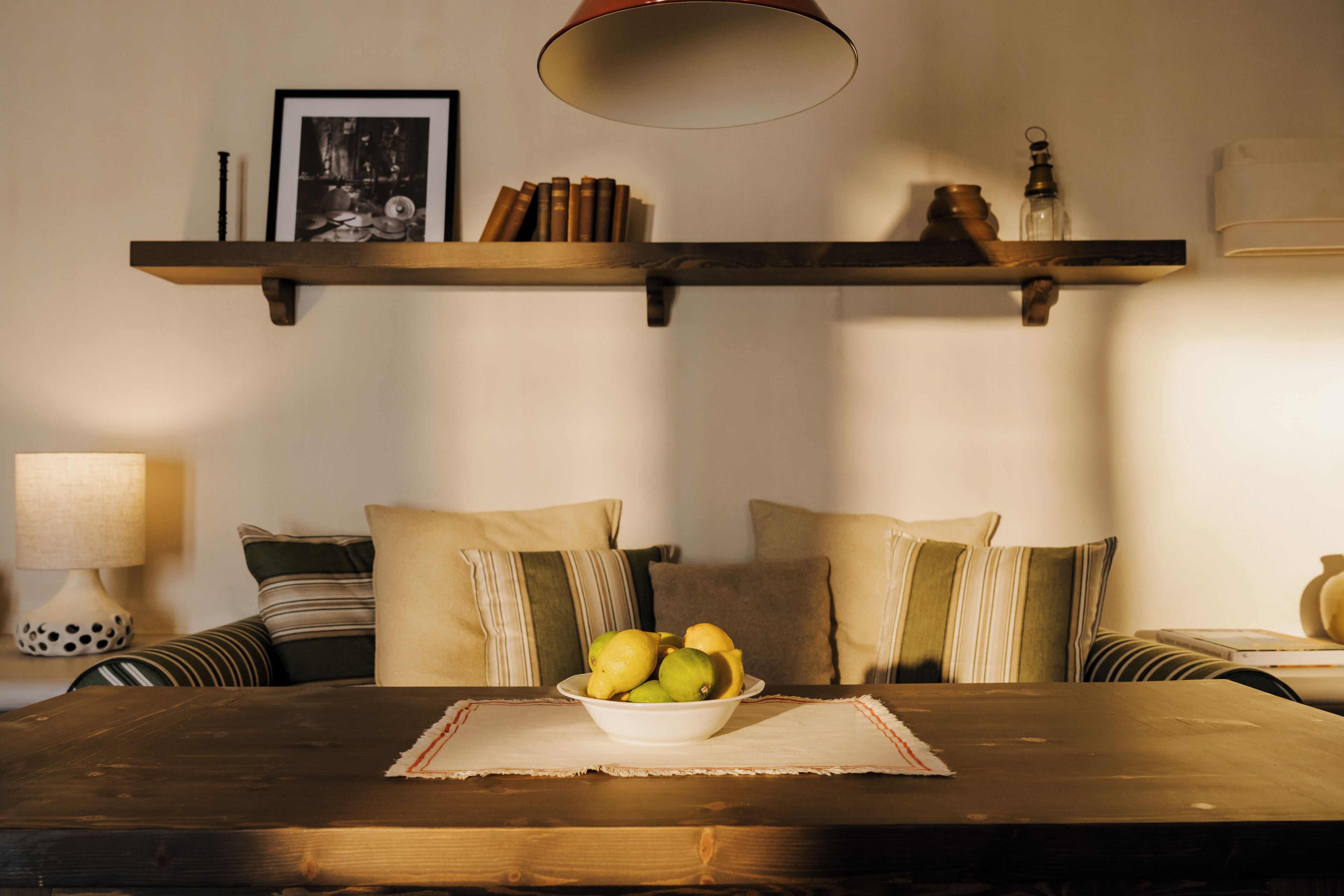 Una habitación acogedora con una mesa de madera, un frutero y una estantería con libros y adornos.