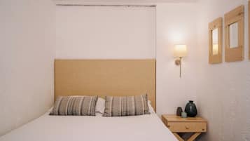 A neatly made bed with patterned pillows, a bedside table with a lamp, and two wall-mounted mirrors.