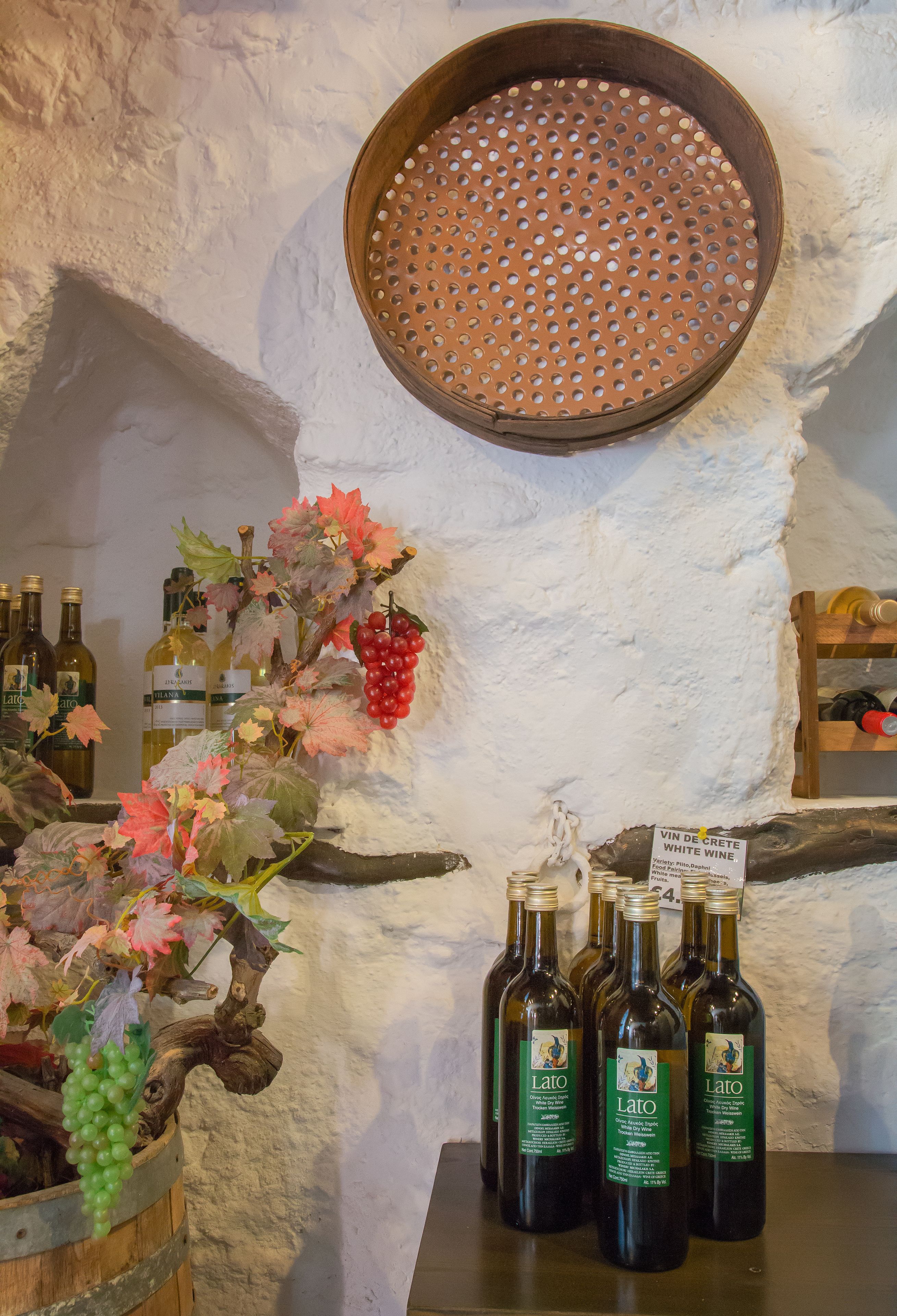 Exhibición de vinos con botellas y parras sobre un muro texturizado.