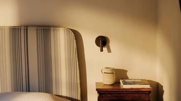 A bed with striped bedding, a bedside table with a book and a vase, and a wall-mounted light fixture.