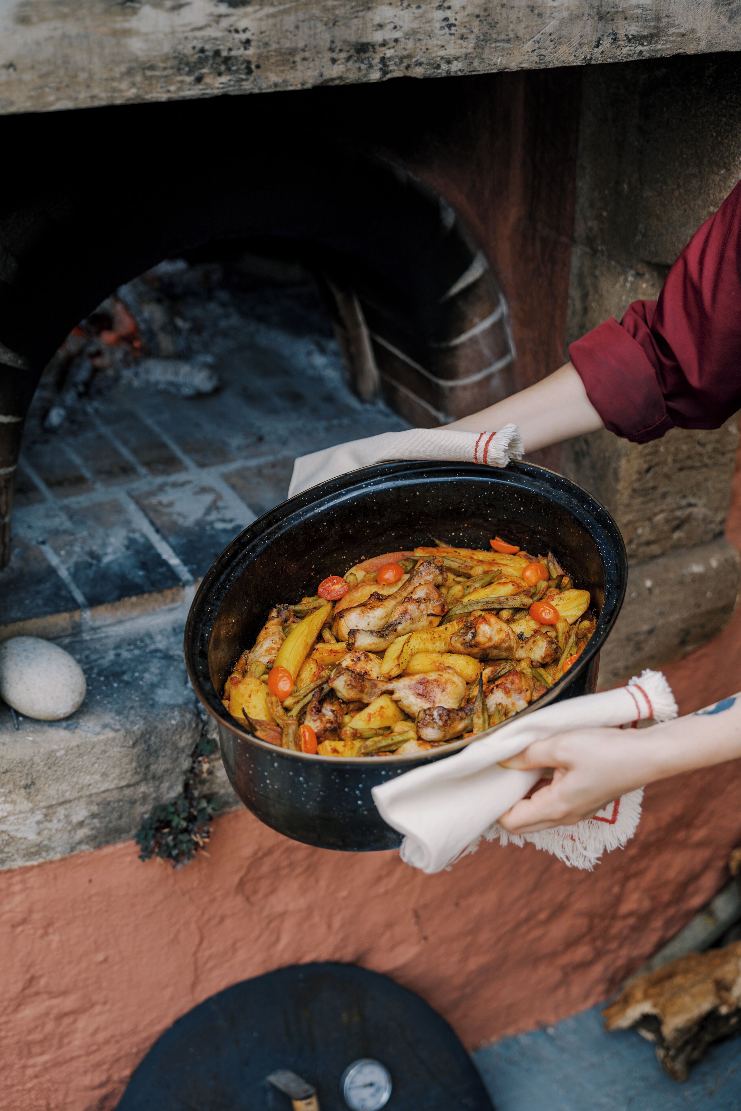 A person holding a large pot of food near a brick oven.