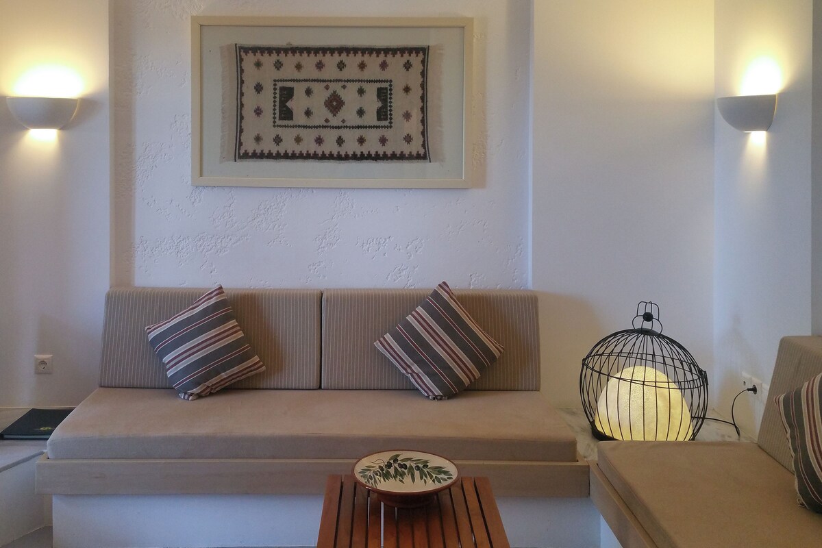 Ein Wohnzimmer mit einer Couch, zwei Kissen, einem kleinen Tisch mit einer Schale, einem Fernseher und Wandleuchten.